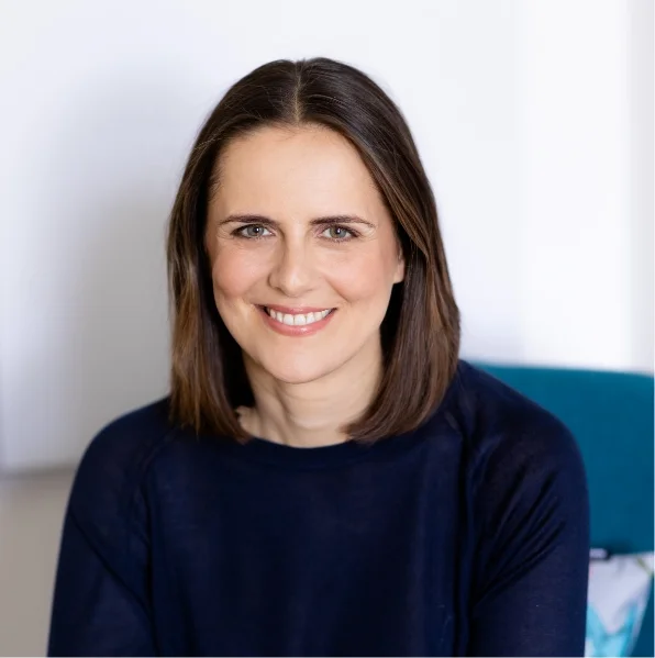 Frau mit dunklem Oberteil lächelt in heller Umgebung.